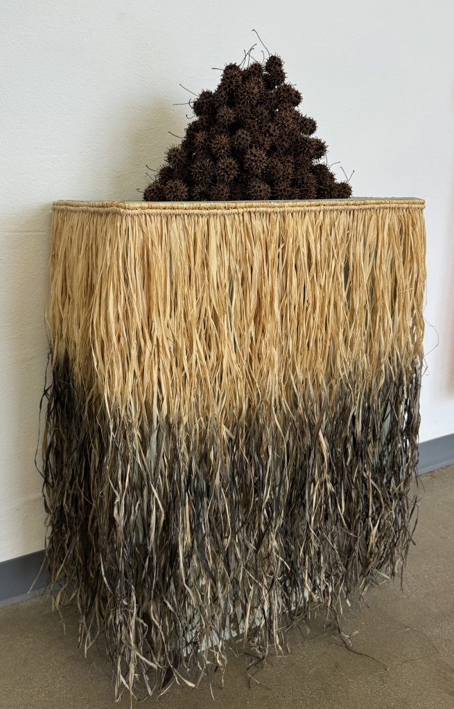 A loose pyramid of sweetgum balls sits on top of a pedestal with a raffia skirt
