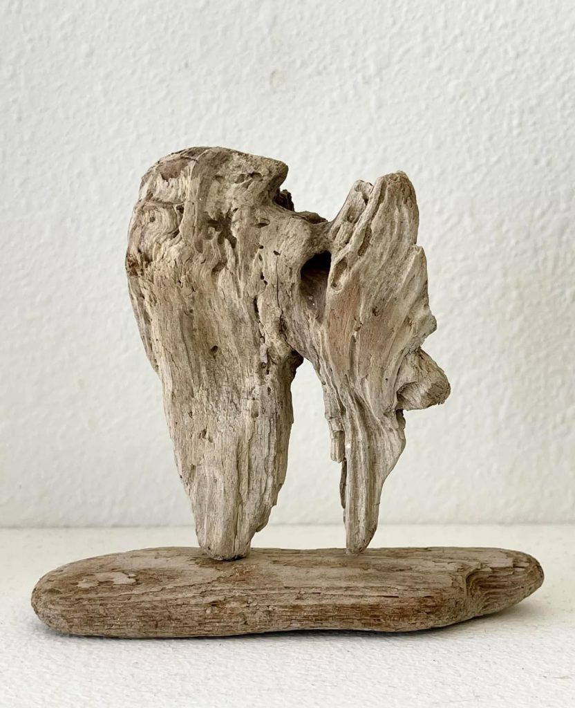 Small sculpture of a piece of driftwood standing up on a horizontal driftwood base
